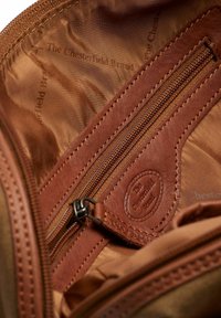 Interno di un portafoglio in pelle marrone con una tasca con zip e rivestimento in tessuto. Presenta un logo impresso e dettagli cuciti sulla pelle.