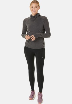 Langärmliges, dunkelgraues Sportoberteil mit Häkelkragen, kombiniert mit schwarzen Leggings und rosa Sneakers, die ein Logo auf den Hosen aufweisen.