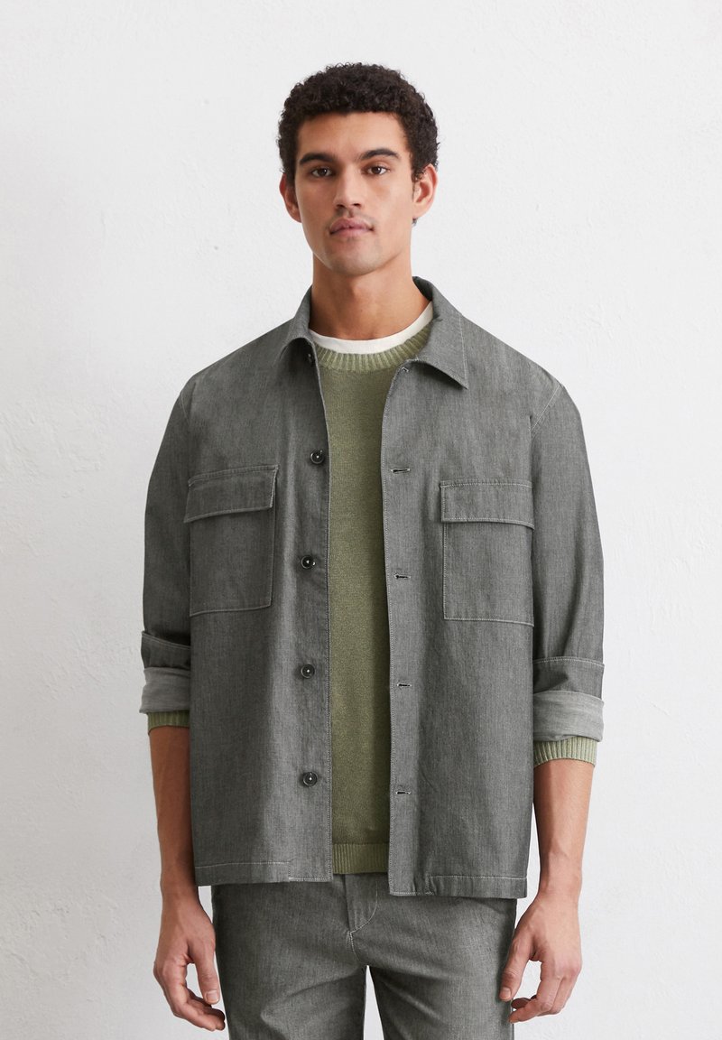 Gray button-up shirt with two front pockets, worn over a green sweater. The shirt has a relaxed fit and rolled-up sleeves. Smooth texture.