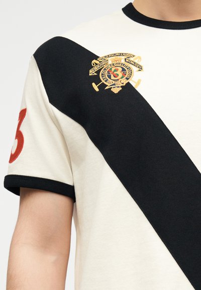 Κρεμ και μαύρο κοντομάνικο πουκάμισο με διαγώνιες ρίγες, κόκκινος αριθμός 3 στο μανίκι και κεντημένο έμβλημα Polo Ralph Lauren στο στήθος.