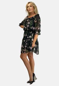 Kwitkowa czarna sukienka z szyfonu z warstwową spódnicą, falbaniastym dekoltem i przezroczystymi rękawami. Noszona z czarno-białymi koturnami.