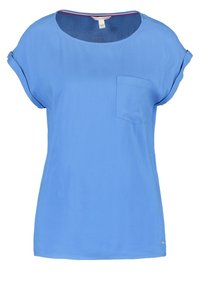 Blusa corta de manga corta azul claro con cuello redondo, que presenta un bolsillo en el pecho y un sutil borde en contraste a lo largo del cuello interno. Tejido suave.
