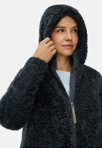 Mørkegrå hættefleecejakke med blød tekstur og en for-lynlås. Har en høj krave og en afslappet pasform.