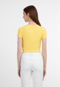Sárga, rövid ujjú crop top ribbed anyagból, kerek nyakkivágással. Fehér, magas derekú farmernadrággal párosítva, amely elegáns formát mutat.