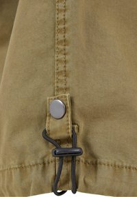 Khaki tkanina s texturovaným povrchem, obsahující kovový knoflík a nastavitelné stahování na lemu, zvýrazněná kontrastními švy.