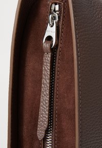 Sac en cuir marron avec un extérieur texturé, une fermeture éclair lisse et un intérieur en daim avec un tirette de zip.