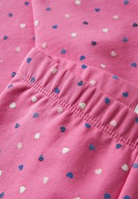 Roze stof met kleine blauwe en witte hartpatronen en zichtbare stiksels van de elastische tailleband.