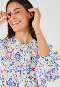 Blusa multicolore con un motivo floreale e geometrico in blu, rosa e verde. Maniche a sbuffo e colletto alla cinese con dettagli in bottone.