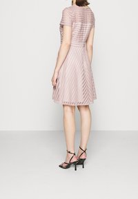 Różowa, dziana sukienka z krótkimi rękawami, z paskowanym wzorem i rozkloszowaną spódnicą; połączona z czarnymi sandałami na wysokim obcasie z paskami.