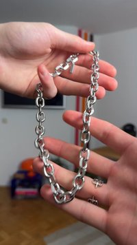 Sølvkæde med sammenlåste ovale og runde led, der viser en poleret finish og en central låsedetalje, holdt i hænder.