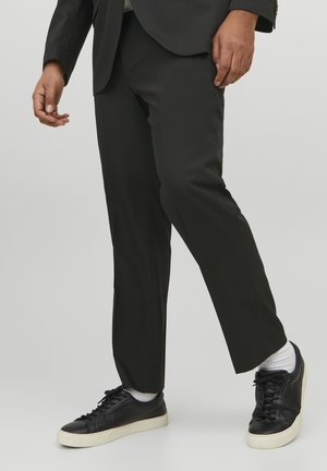 Schwarze maßgeschneiderte Hosen kombiniert mit schwarzen Ledersneakern mit weißen Sohlen und Schnürsenkeln sowie sichtbaren weißen Socken.