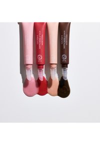Quatre tubes de baume à lèvres Soft'n Tinted de GOSH en rose, rouge, nude et marron avec des échantillons de baume à lèvres assortis sous chaque tube sur une surface blanche.