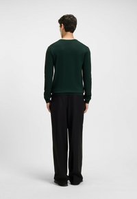 Grüner Longsleeve-Pullover mit geripptem Kragen und Bündchen, kombiniert mit schwarzen weiten Hosen. Der Stoff wirkt glatt, mit einer figurbetonten Silhouette.