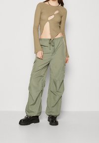 Khaki lange mouwen top met uitsnijding, gecombineerd met lichtgroene cargobroeken. Zwarte platform schoenen maken de outfit af.