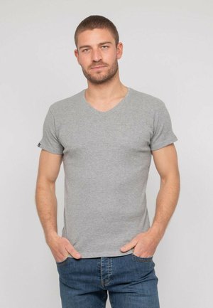 T-shirt gris en coton doux, col en V, manches courtes, coupe ajustée ; associé à un jean en denim bleu, les mains dans les poches.