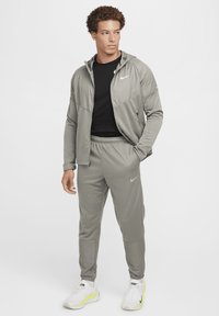 Harmaa Nike-treenihaalari, jossa on huppari ja joustavat housut. Varustettu tekstuurilla, mustalla t-paidalla alla ja valkoisilla tennareilla.