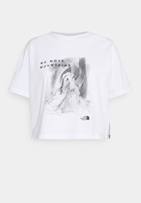 Camiseta blanca recortada de algodón, con una ilustración gráfica negra que incluye el texto "WE MOVE MOUNTAINS" y un logo en el dobladillo.