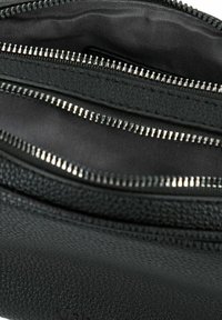 Interno di una borsa in pelle nera dalle texture, con più scomparti con cerniera e una fodera liscia in tessuto scuro. Le cerniere presentano dettagli metallici.