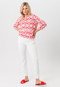 Rood en wit gebreid sweater met een losse pasvorm, gecombineerd met witte broek en rode slide-sandalen. Soepele stof met een geometrisch patroon.