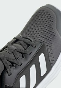 Grauer Sportschuh mit einem Obermaterial aus Mesh und Lederakzenten. Weiße Streifen an der Seite und strukturierte Schnürsenkel fügen Details hinzu. Gummisohle sichtbar.
