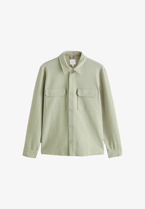 Gaiši zaļa pogājama krekla jaka ar divām priekšējām kabatām ar atlokiem un garām piedurknēm, attēlota uz balta fona.