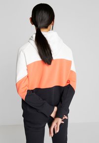 Sudadera con capucha en blanco, coral y negro. Presenta un diseño de bloques de color, tejido suave, bolsillo frontal y puños acanalados.