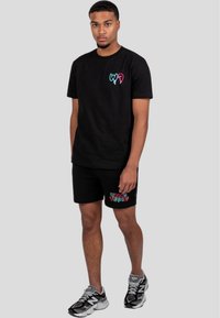 Sort bomulds T-shirt med farverige grafiske detaljer på brystet; sorte shorts med multicolore teksttryk; iført sporty sneakers.