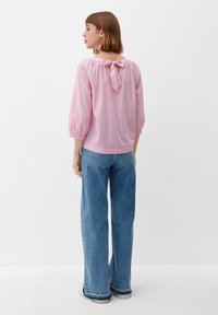 Roze blouse met een strikdetail op de rug, met pofmouwen en een iets lose fit, gecombineerd met brede blauwe denim jeans.