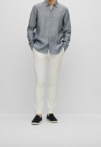 Grå skjorta med knappar och strukturerad väv, vita slim-fit-byxor och svarta slip-on-skor. Halvlånga ärmar och avslappnad passform.