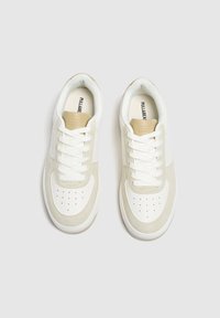 Białe i beżowe sneakersy z gładkim skórzanym noskiem, zamszowymi akcentami, płaskimi sznurówkami, wyściółką amortyzującą oraz perforowanymi detalami na nosku.