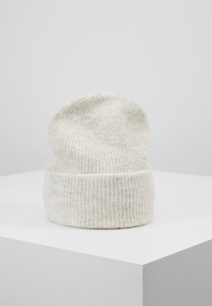 Zachte, geribbelde gebreide wintermuts in off-white kleur, tentoongesteld op een wit voetstuk tegen een effen achtergrond.