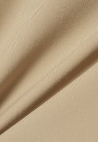 Tissu beige à texture fine et plis doux, montrant des variations de lumière et d'ombre sur la surface.