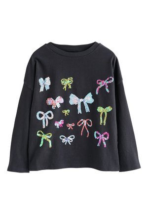 Zwart shirt met lange mouwen, versierd met diverse kleurrijke, met pailletten bezaaide strikken in verschillende maten en ontwerpen aan de voorkant.