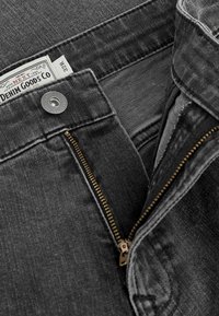 Šedé džíny z denimu se zlatým zipem, zapínáním na knoflík a tkanou značkovou etiketou. Obsahují vyšitý detail podél pásku a kapes.