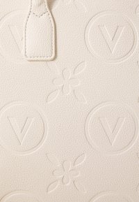 Cuir blanc texturé avec des motifs floraux et de logo en relief. Présente une petite étiquette rectangulaire avec un bord cousu.