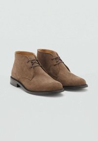 Stivaletti alla caviglia in suede marrone con design di lacci sottili, punta arrotondata e tacco nero basso. Texture liscia e silhouette minimalista.