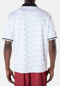 Witte polo shirt met korte mouwen en een reliëfpatroon met "MIAMI." Zwarte kraag en mouwaccenten. Klassieke pasvorm en textiel met een structuur.