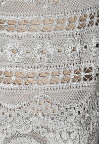 Grå virkad tyg med invecklade mönster, genombrutna detaljer och texturerade nyanser. Olika stygnmönster skapar ett lagerutseende.