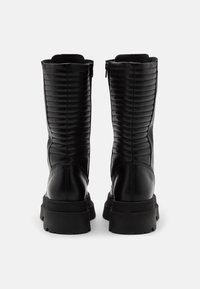Bottes noires pour cheville en matériau synthétique matelassé, avec une semelle épaisse et des fermetures éclair à l'arrière. Texture lisse avec un design élégant.