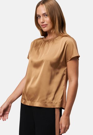 Haut court en satin bronze à manches courtes avec un col rond, des fentes latérales et une texture lisse. Porté avec un pantalon noir présentant un accent contrasté.