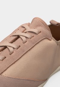 Ανοιχτοροζ αθλητικό παπούτσι με πάνελ από σουέντ και λείο ύφασμα, επίπεδα κορδόνια και θηλιά στην φτέρνα, εμφανιζόμενο σε κοντινή λήψη.