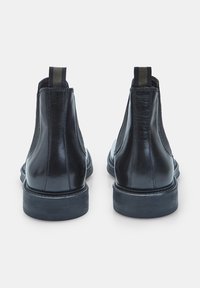 Botas de cuero negro hasta el tobillo con paneles laterales elásticos, suelas planas y lengüetas, que presentan un acabado suave y un diseño de punta redondeada.