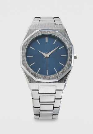 Zilverkleurig metalen polshorloge met een blauw rond gezicht, minimalistische uurmarkeringen en een metalen schakelen armband, die de tijd 10:10:30 weergeeft.