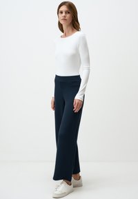 Witte langermige geribbelde top gecombineerd met marineblauwe geribbelde brede broek en witte sneakers, toont een getailleerd silhouet en gestructureerde stof.