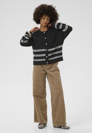 Cardigan en laine noir avec des rayures blanches, des boutons dorés et une coupe décontractée ; associé à un pantalon en velours côtelé beige à jambes larges et des chaussures à imprimé zèbre.