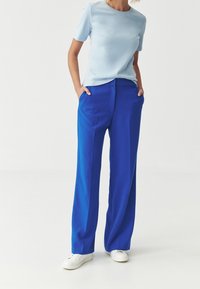 Jasnoniebieski top z krótkim rękawem w połączeniu z szerokimi spodniami w kobaltowym odcieniu, o gładkiej fakturze i dwoma bocznymi kieszeniami. Całość uzupełniają białe trampki.
