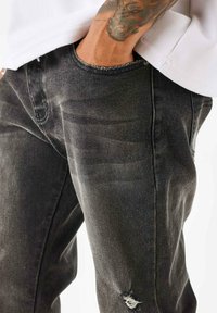 Zwarte denim jeans hebben een verouderd detail bij de zoom, met een vervaagde textuur. Ze hebben een klassiek vijf-pocket ontwerp.