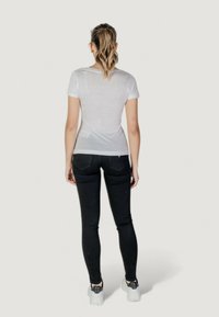 T-shirt blanc ajusté à manches courtes, associé à un jean skinny noir et des baskets grises. Tissu lisse et design épuré sans motifs visibles.