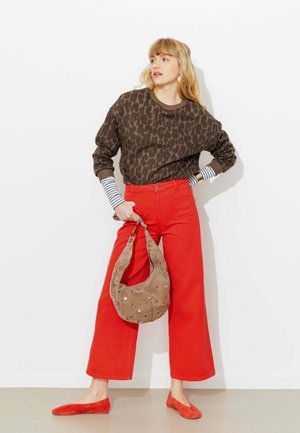 Femme portant un pull à imprimé léopard, un pantalon large rouge, des ballerines rouges assorties, des manches rayées, tenant un sac à bandoulière marron clouté.