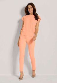 Helles korallenfarbenes, strukturiertes Oberteil mit kurzen Ärmeln, kombiniert mit hellen korallenfarbenen Skinny-Jeans, die ausgefranste Säume und Schlangenleder-Print-Absätze aufweisen.